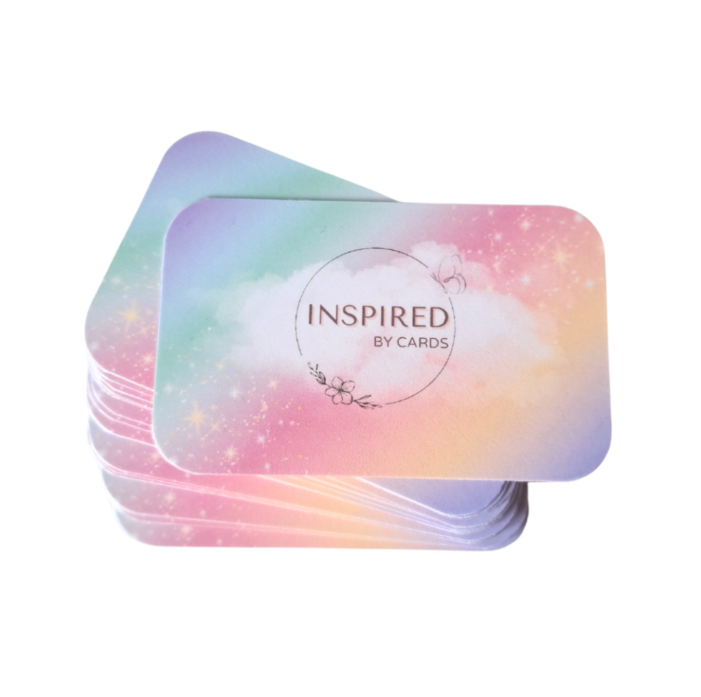Een stapel kleurrijke kinderaffirmatiekaarten van More2Inspire. De affirmatiekaarten voor kinderen hebben een vrolijk regenboogkleurig ontwerp. Op de bovenste affirmatiekaart voor kinderen is de tekst "Inspired by Cards"zichtbaar. Het affirmatiekaartje komt uit een kaartenset van More2Inspire.