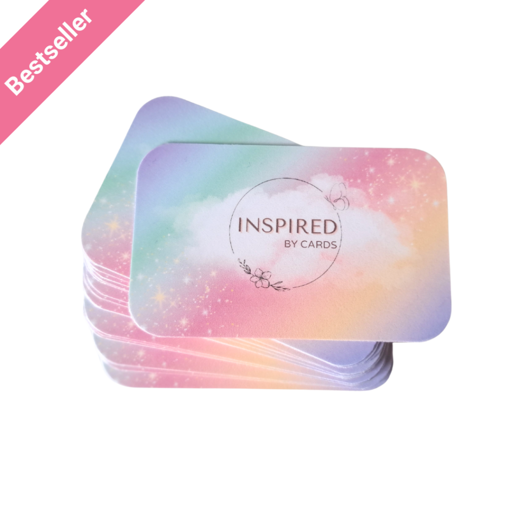 Een stapel kleurrijke kinderaffirmatiekaarten van More2Inspire. De affirmatiekaarten voor kinderen hebben een vrolijk regenboogkleurig ontwerp. Op de bovenste affirmatiekaart voor kinderen is de tekst "Inspired by Cards"zichtbaar. Het affirmatiekaartje komt uit een kaartenset van More2Inspire. In de linkerbovenhoek is een roze kleurig label zichtbaar met de tekst "beststeller".